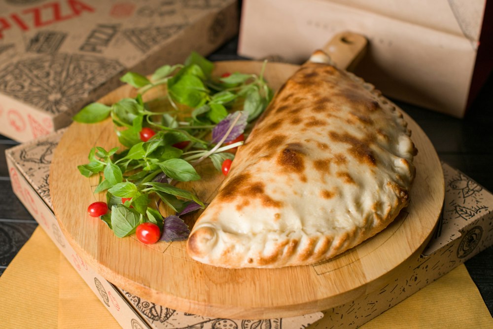 Un calzone dorado sobre una tabla de madera con ensalada